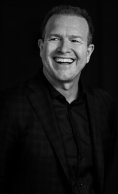Corporate headshot in black and white of a man wiht a wide smile